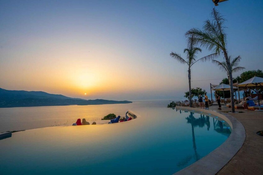 A sunset over a calm sea with a pool and palm trees. 1