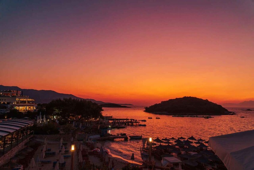 A sunset over a coastal town with a beach, boats, and a hill in the distance. 3