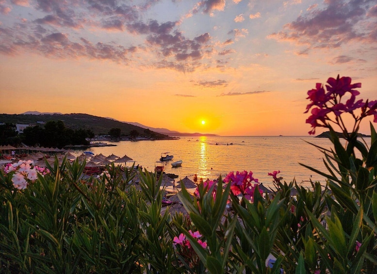 A sunset over a calm sea with boats, beach umbrellas, and a mountainous backdrop. 2