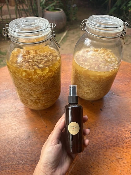 Two glass jars filled with a golden liquid, a small dark bottle with a label, and a wooden table. 5