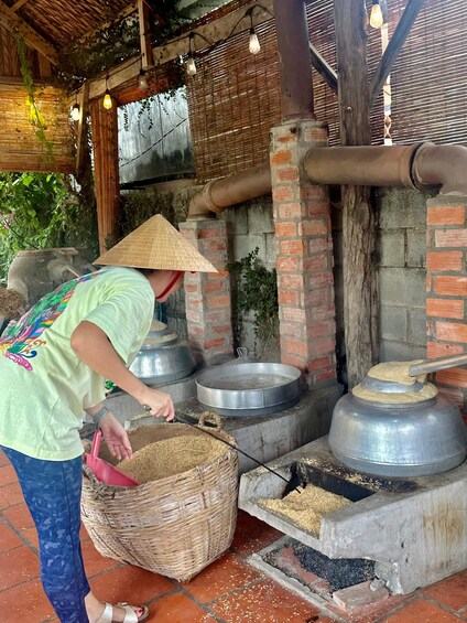 A person in a conical hat handling a basket near traditional cooking equipment. 2