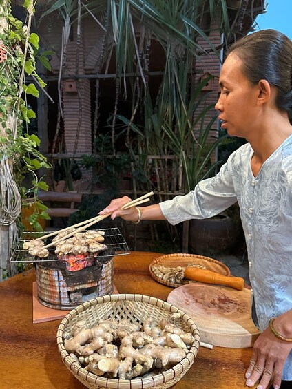 A person grilling ginger on a charcoal grill outdoors with a basket of ginger in front of them. 4