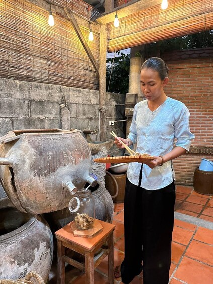 A person cooking outdoors with a large clay pot and a smaller pot on a table. 5