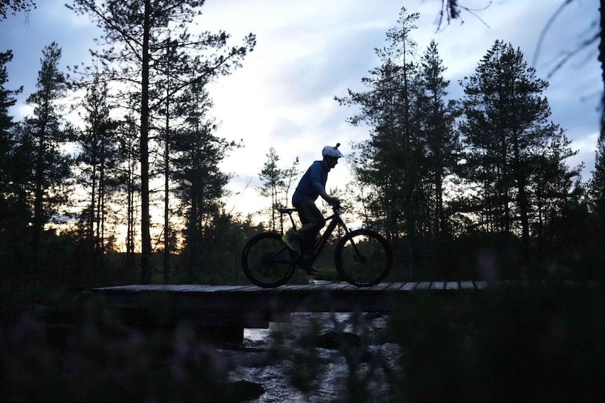 A person on a mountain bike performing a jump over a bridge in a forested area. 2