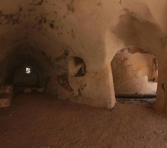 An ancient, dimly lit underground passage with arched ceilings and a small window at the far end. 4