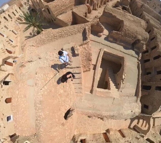 An ancient ruin with stone structures and a palm tree. 2