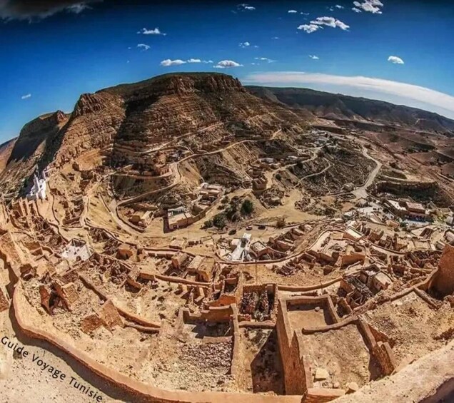 A panoramic view of a desert landscape with ancient ruins and a mountain in the background. 1