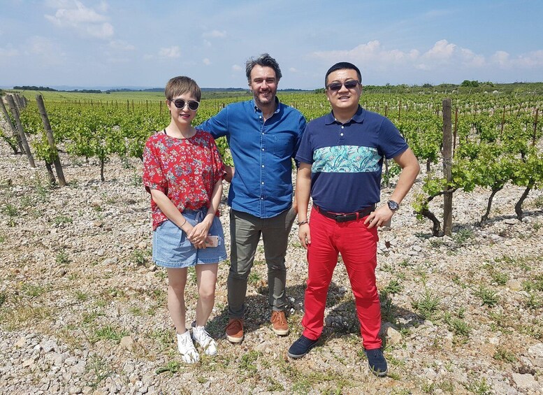 Three people standing in a vineyard with rows of grapevines. 2