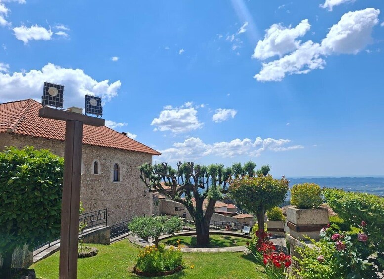 A stone building with a tiled roof, surrounded by lush greenery and a clear blue sky. 4