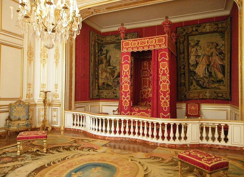 An ornate room with a red and gold throne, a chandelier, and classical paintings. 3
