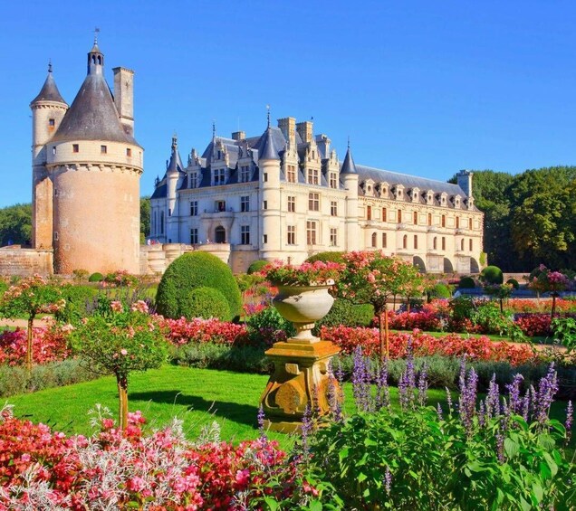 A historic château with a tower, surrounded by a well-manicured garden with various flowers and topiary. 5