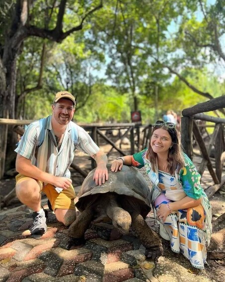 Two people posing with a tortoise on a paved path in a wooded area. 4
