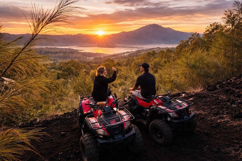 Two people on ATVs overlooking a mountainous landscape with a sunset. 3