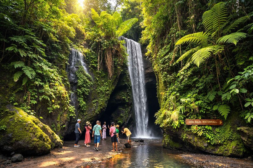A waterfall with people observing and a sign indicating 'GOA RAJA WATERFALL.' 2