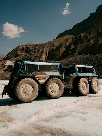 A large, multi-wheeled vehicle with a rugged design, parked on a snow-covered ground with a mountainous backdrop. 4