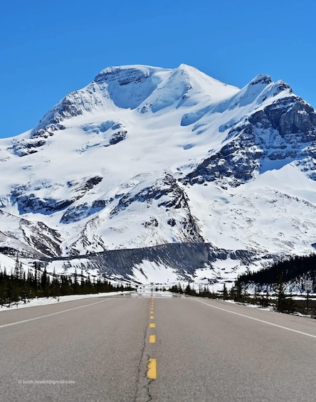 A snow-covered mountain range with a clear road leading towards it. 2