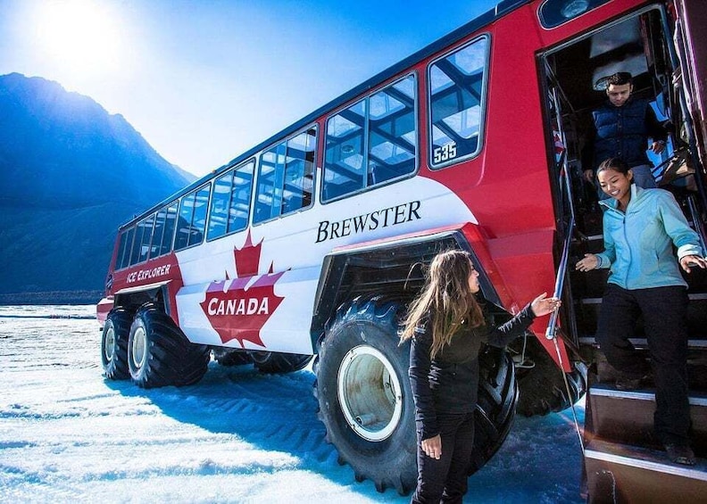 A red and white bus with 'BREWSTER' and 'CANADA' written on it, parked on snow with mountains in the background. 1