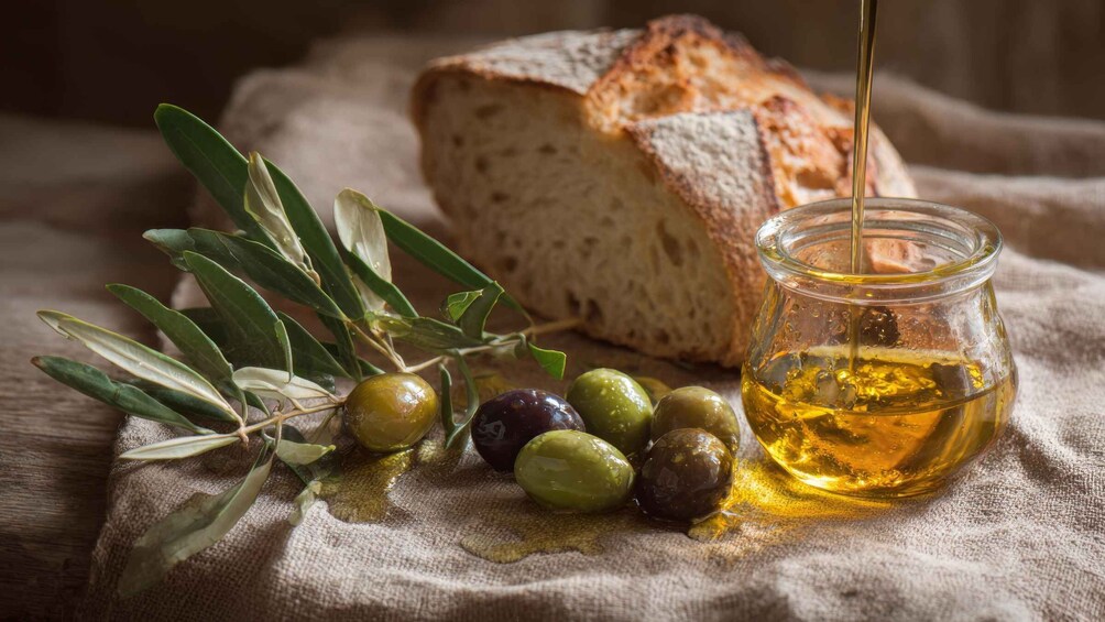 A loaf of bread, olives, olive oil, and olive branches on a cloth. 3