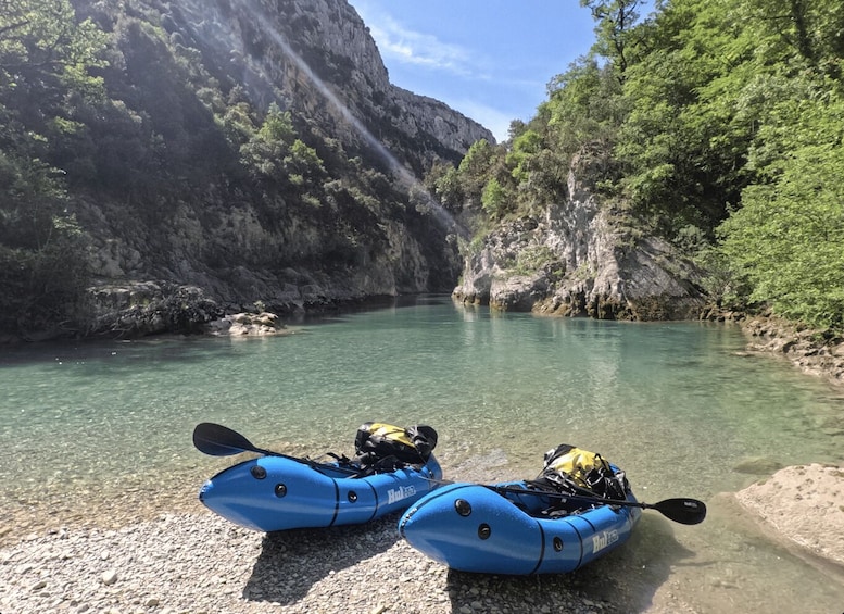 Two blue kayaks on a pebbly riverbank with clear water and rocky cliffs in the background. 5