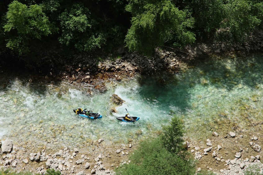 Two kayaks on a clear river surrounded by rocky banks and dense greenery. 2