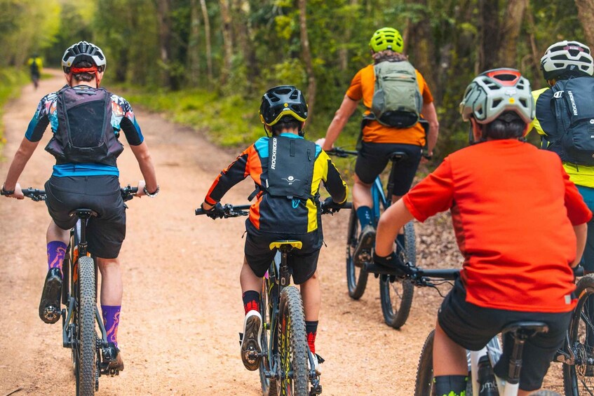 A group of cyclists on a dirt path surrounded by trees. 1