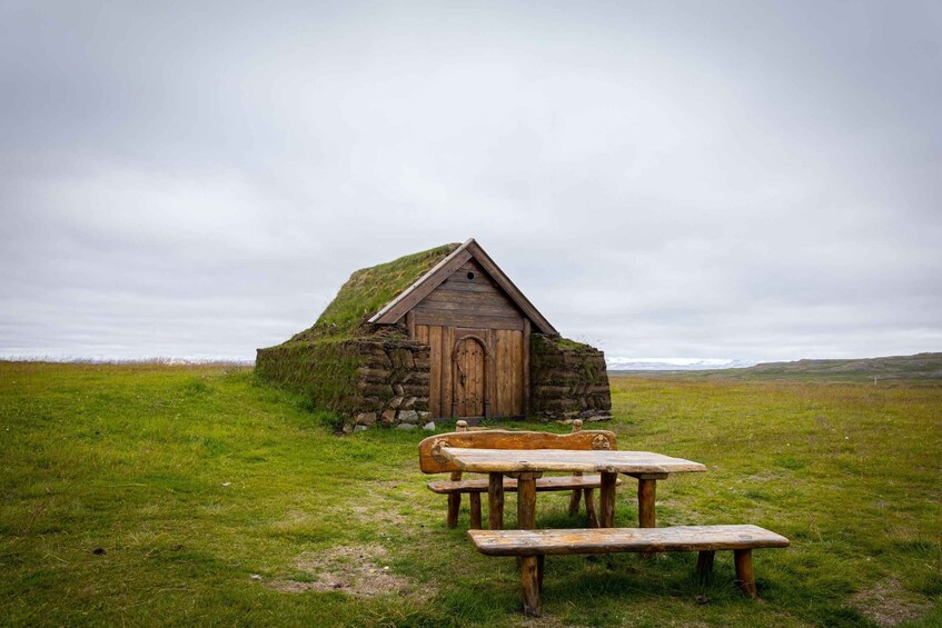 A stone hut with a grass roof and a picnic table in a grassy field. 5