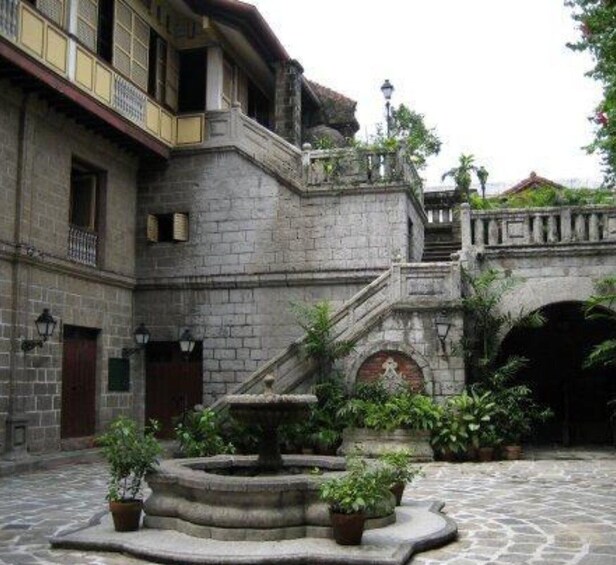 Un patio con una fuente de piedra, plantas en macetas y un edificio tradicional con balcón. 5
