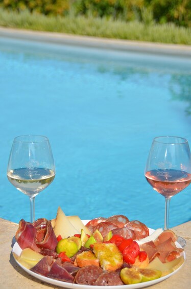 A charcuterie board with various meats and cheeses by a poolside. 1