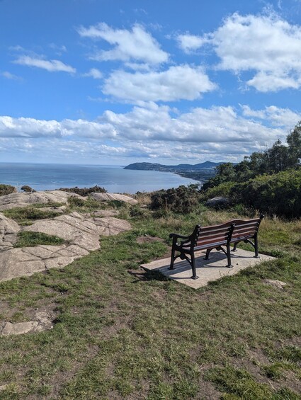 A bench overlooking a coastal landscape with rocky terrain and distant hills. 2