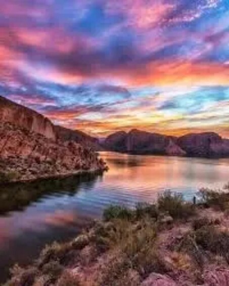 A sunset over a calm lake with rocky terrain and mountains in the distance. 1