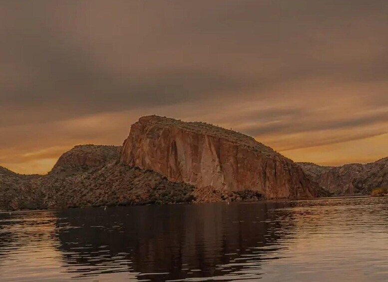 A large rock formation by a calm body of water during sunset. 3