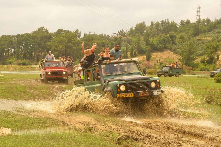 A group of people on a green off-road vehicle driving through a muddy field. 4