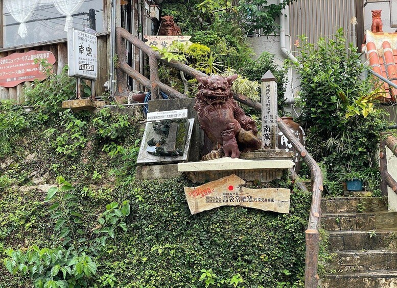 A stone lion statue at the base of a staircase, surrounded by greenery and various signs. 2