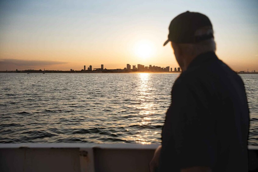 A person standing on a boat with a city skyline in the background during sunset. 2