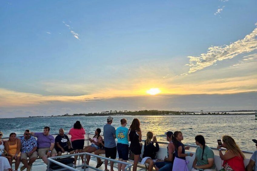 A group of people on a boat at sunset, with the sun setting over the horizon. 3