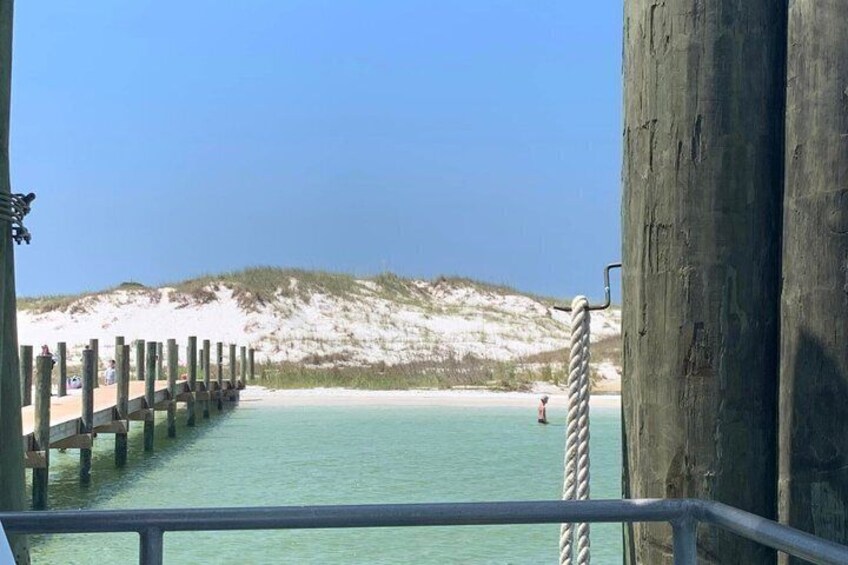 A pier extending into turquoise water with a sandy beach and dunes in the background. 2