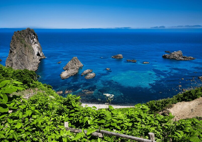 A coastal landscape with a prominent rock formation, clear blue sea, and lush greenery. 4