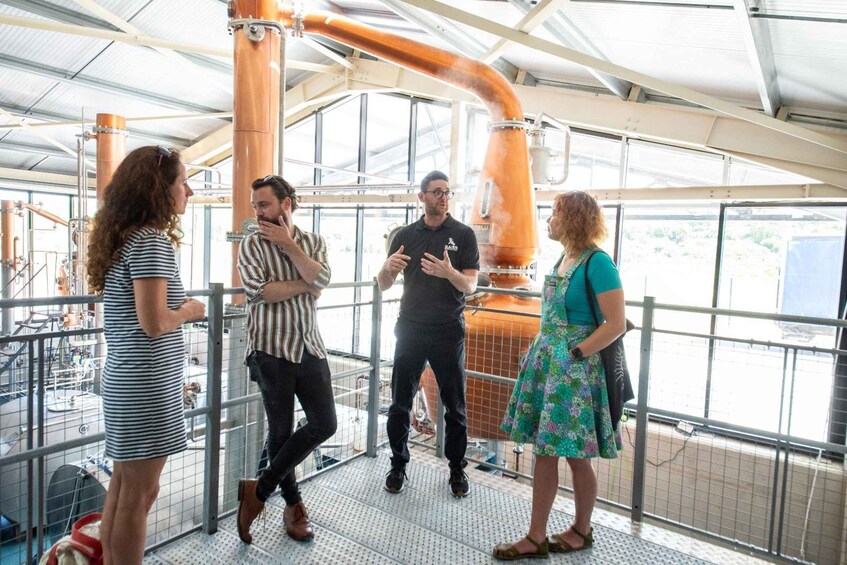 A group of people standing on a metal platform inside a building with industrial equipment and large pipes. 5