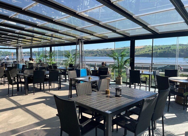 An outdoor dining area with tables and chairs, overlooking a body of water and greenery. 4