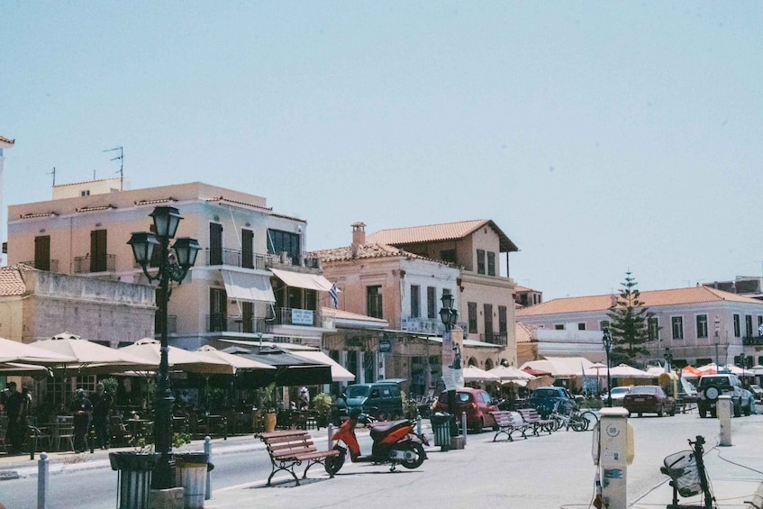 A street with parked cars, a scooter, and outdoor seating at cafes. 1
