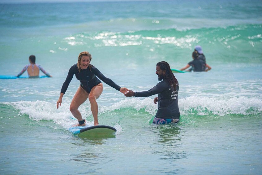 Two people surfing on a wave with others in the background. 3