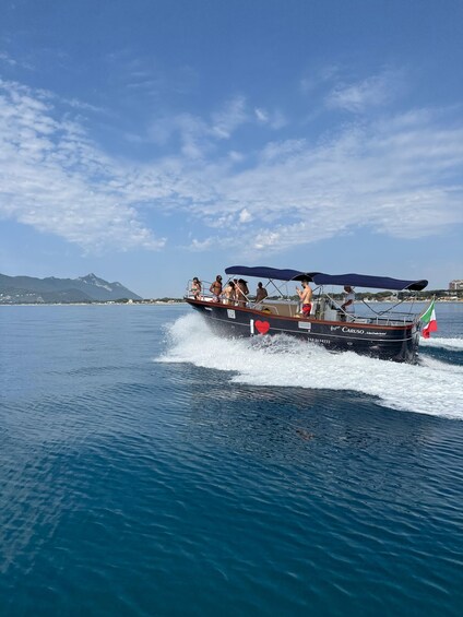 A boat with people on board, moving through a body of water with a mountainous landscape in the background. 5