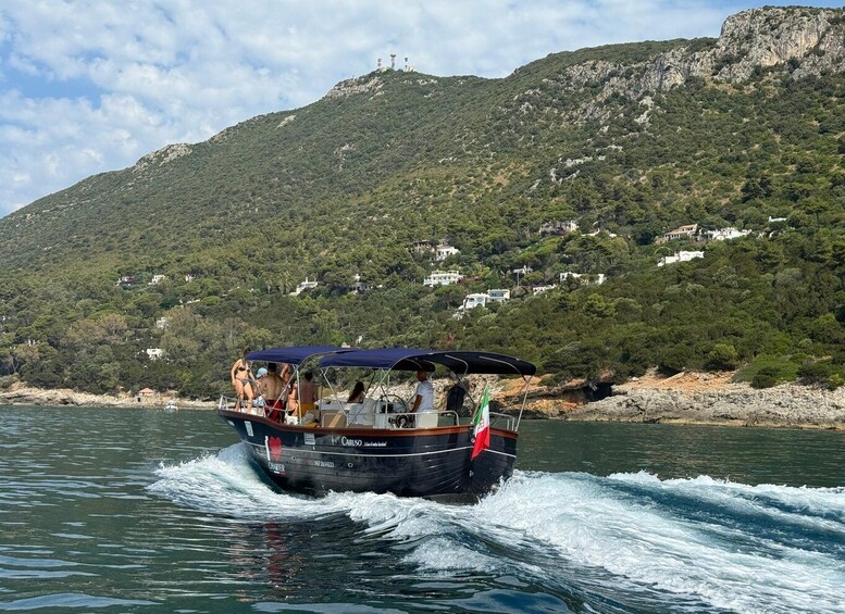 A boat with passengers on a calm sea, surrounded by a mountainous landscape with scattered buildings. 2