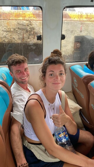 Two people seated in a bus with blue seats and a window showing a rocky landscape. 3
