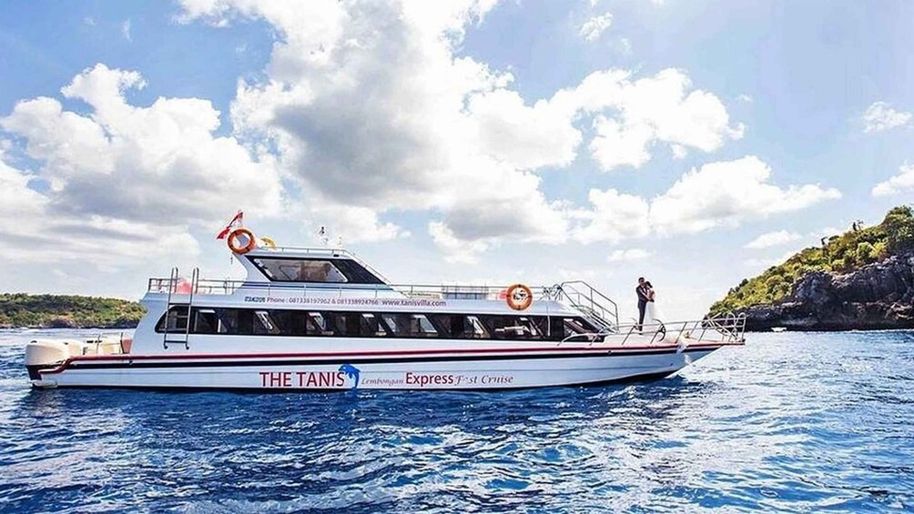 A white boat named 'The Taniis Express First Cruise' on water with a rocky coastline and a partly cloudy sky. 5