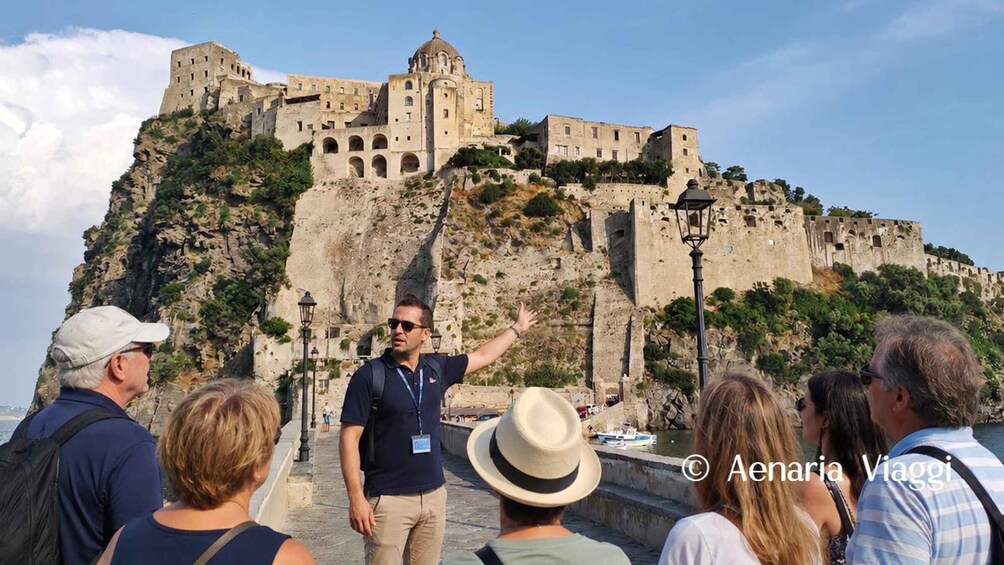 A group of tourists observing a historic fortress on a cliff overlooking the sea. 1