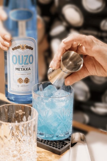 A person pouring a drink from a bottle labeled 'OUZO METAXA' into a glass with ice. 2
