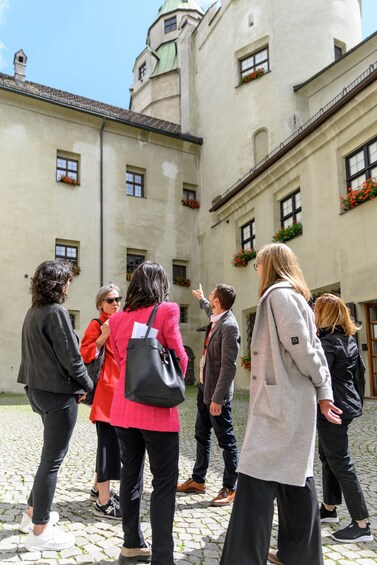 A group of people walking on a cobblestone path in front of a historic building with flower boxes and a tower. 5