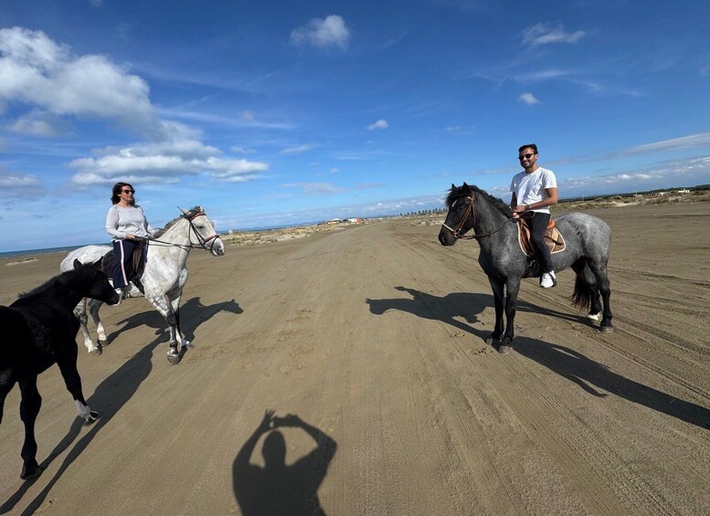 Two people riding horses on a sandy beach with a clear sky. 2
