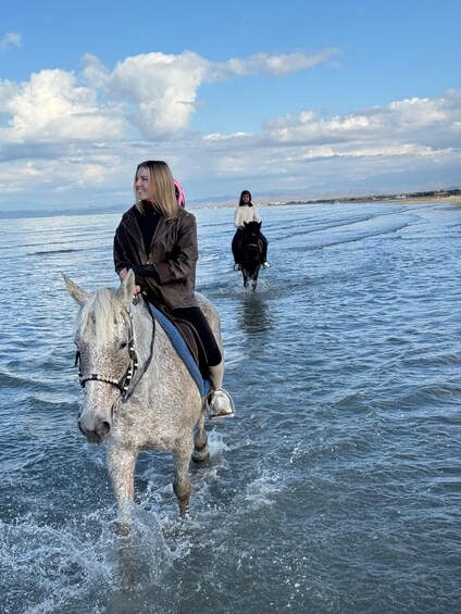 A person riding a horse through shallow water, with a clear sky and distant mountains in the background. 3